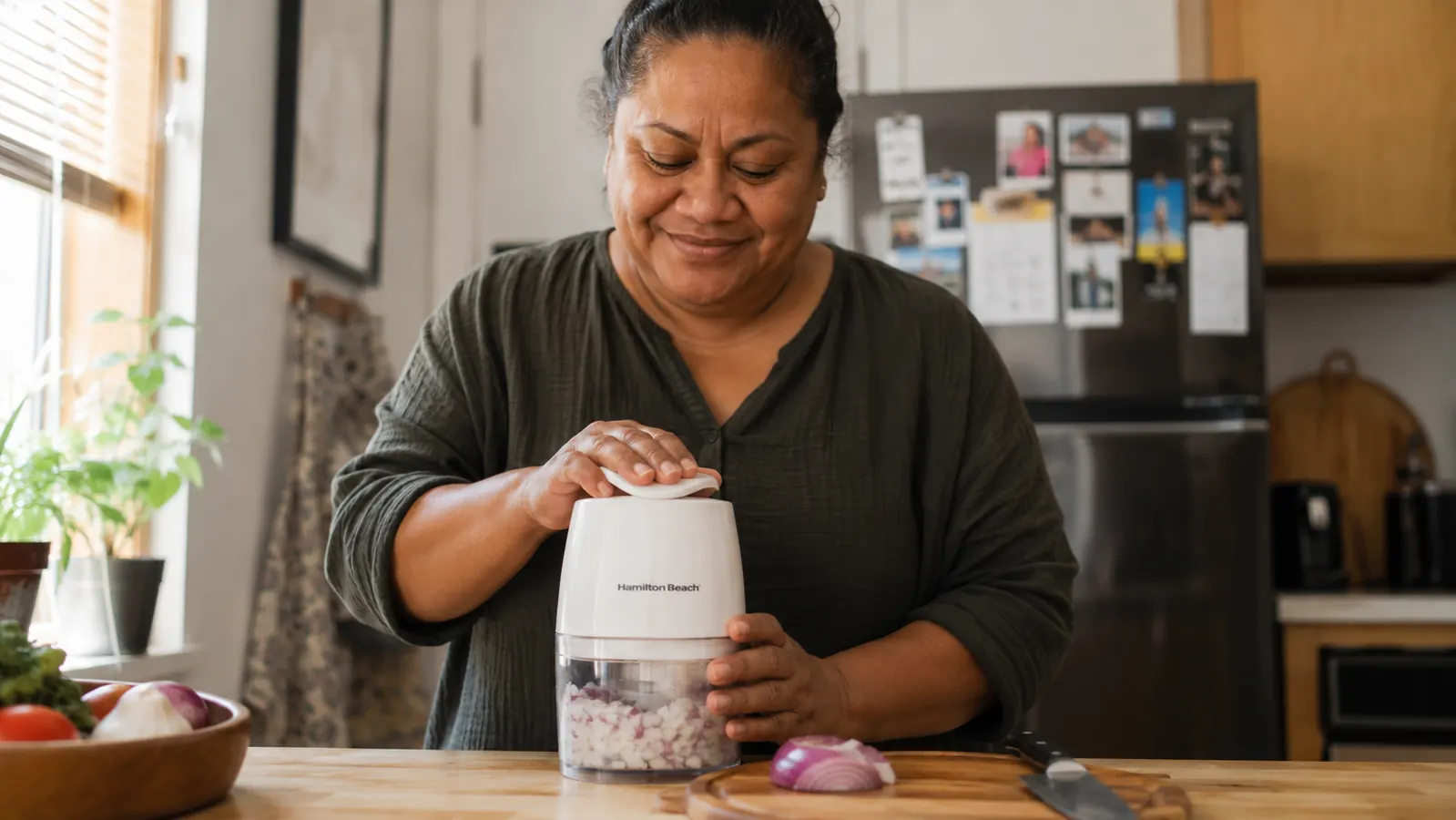 Hand pressing down the lid of a Hamilton Beach food chopper filled with diced onion