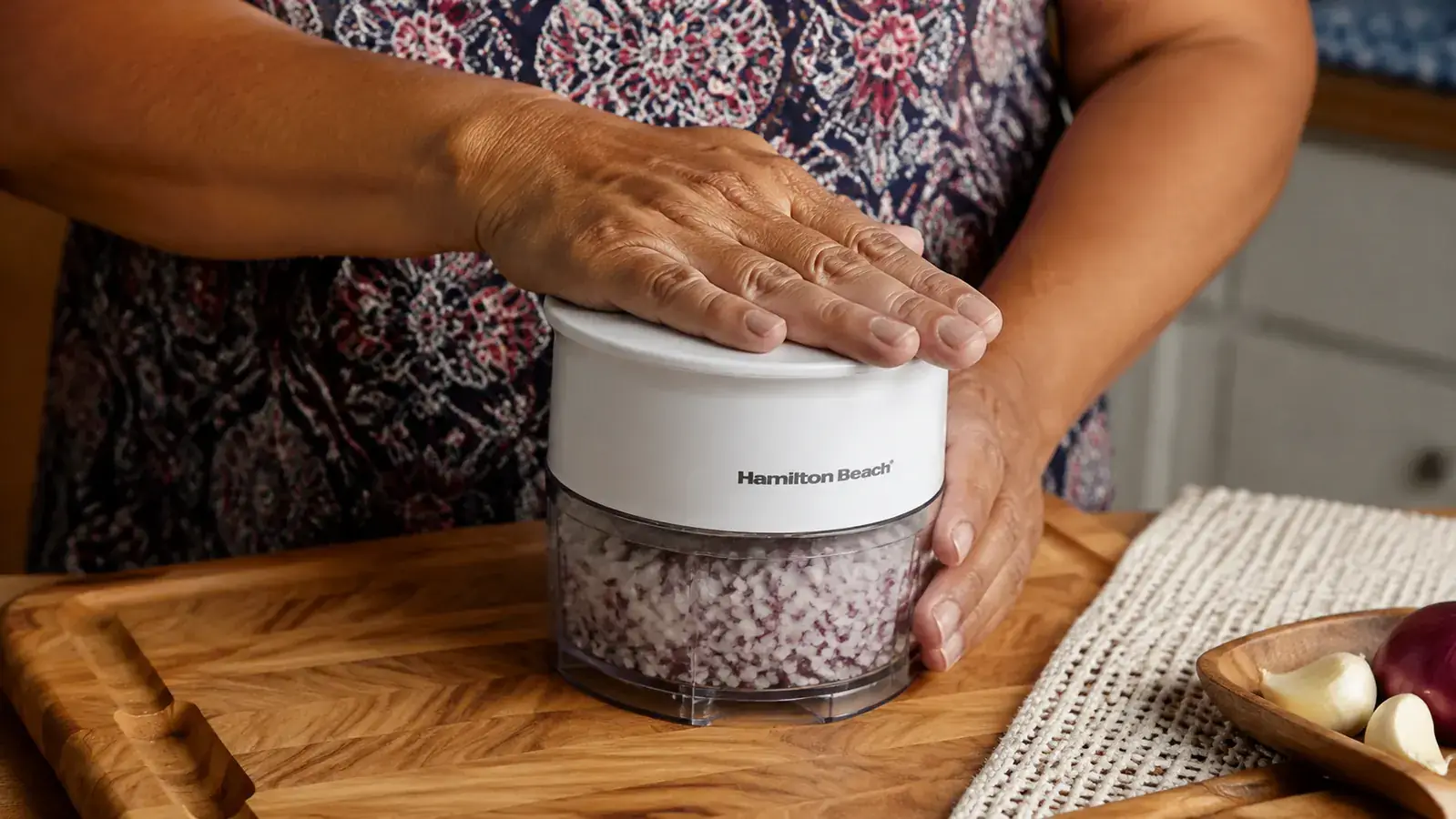 Close-up of the Hamilton Beach food chopper lid being pressed down by a palm to activate the motor