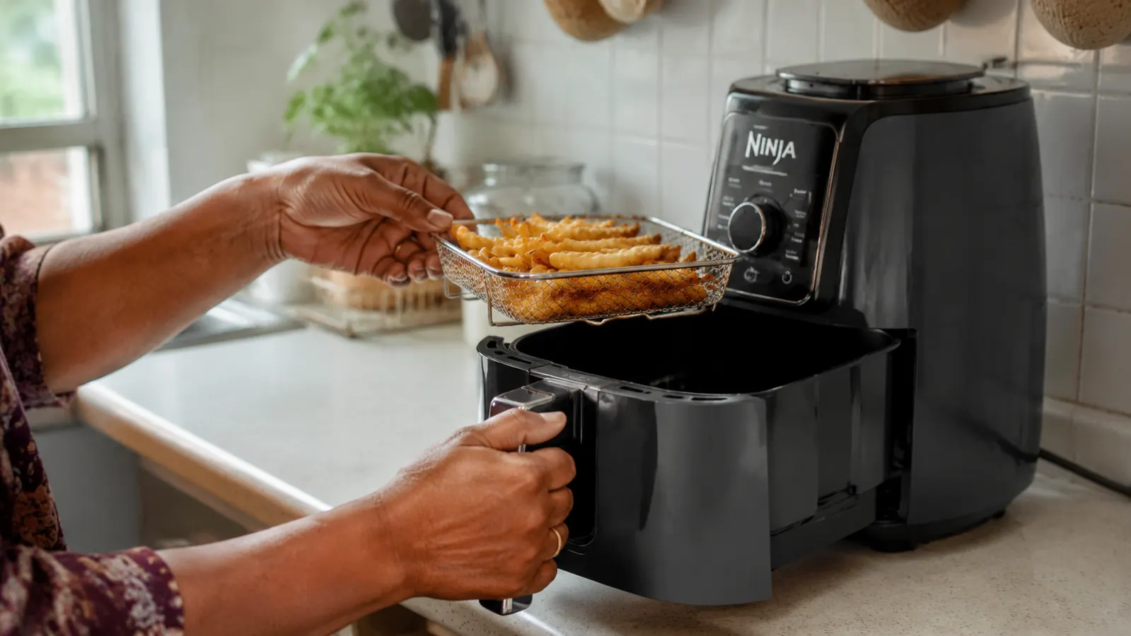 Hand placing leftover French fries into the Ninja Air Fryer basket, basket held at a slight angle