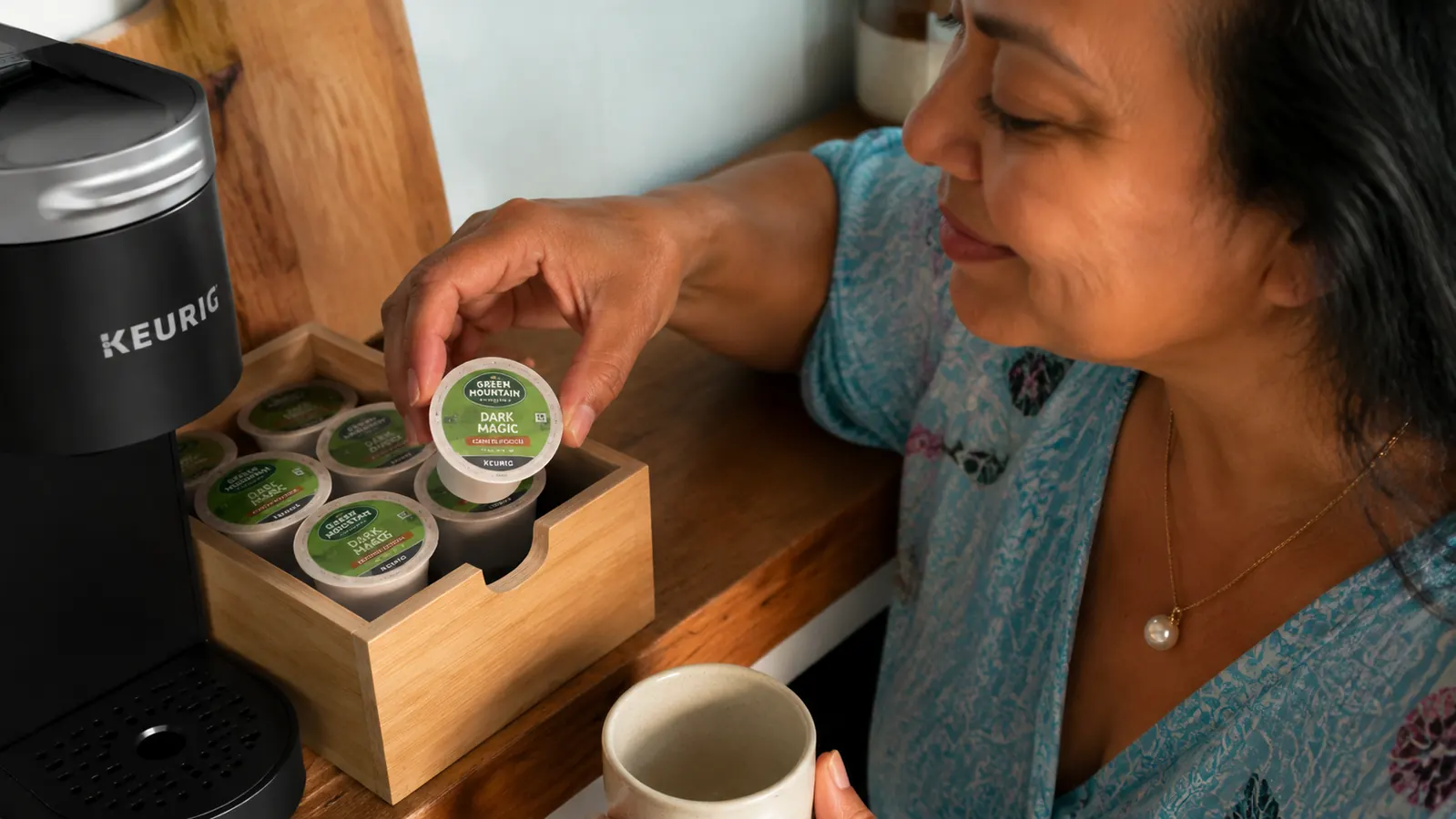 Close-up of K-Cup pods in a small wooden organizer next to the Keurig K-Mini, showing variety of roast options