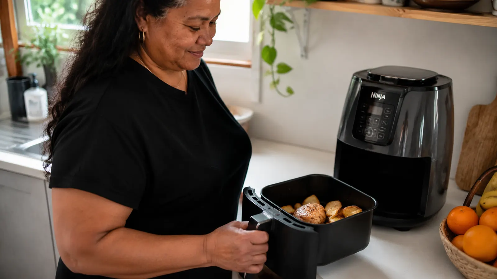 Ninja air fryer basket removed and sitting beside the unit with a single chicken thigh and two small potato wedges inside