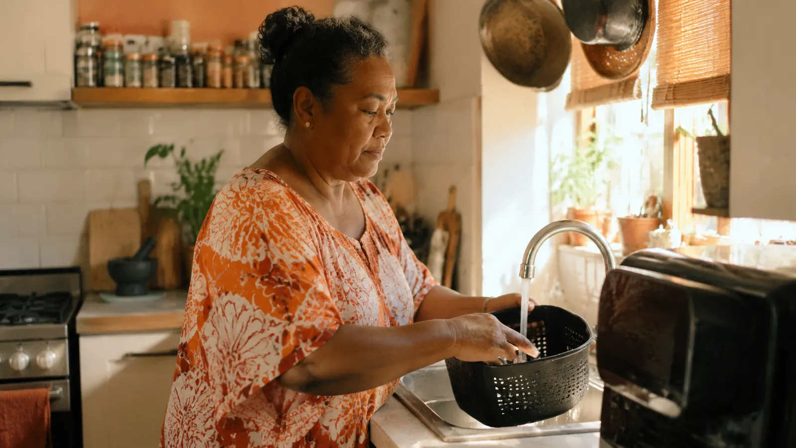 Caregiver cooking a small meal in a tidy apartment kitchen, air fryer basket sitting open on the counter ready to be cleaned